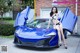 A woman in a bikini sitting on top of a blue sports car.