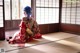 A woman in a red kimono sitting on a tatami mat.