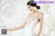 A woman in a wedding dress sitting in front of a wall of paper flowers.