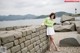 A woman leaning against a stone wall by the water.